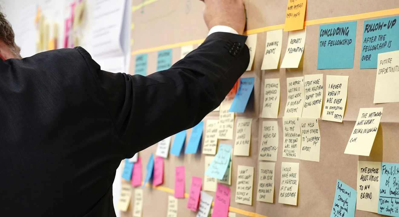 man writing on board filled with sticky notes
