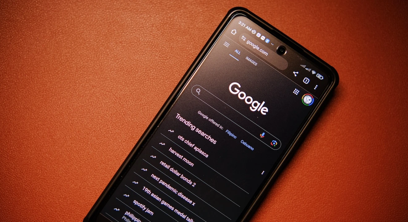 Smartphone displaying the Google Search homepage in dark mode, with trending search results visible on the screen