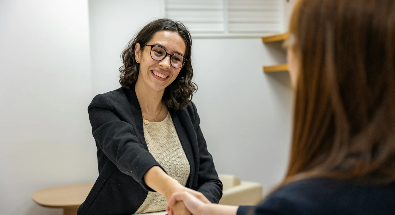 a woman shaking hands with another woman sitting at a table