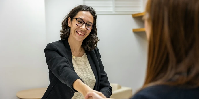 a woman shaking hands with another woman sitting at a table